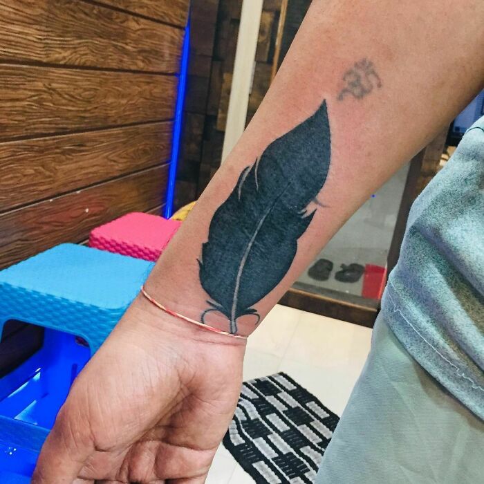 Feather wrist tattoo in black ink, showcasing bold design.