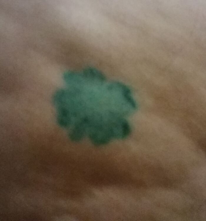 Blurry green tattoo resembling a small floral shape on skin.