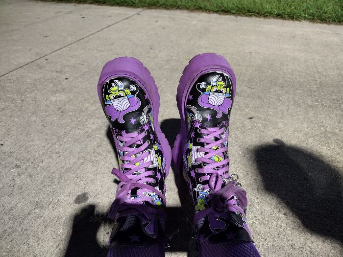Quirky pair of purple boots with cartoon characters on a sunny sidewalk.