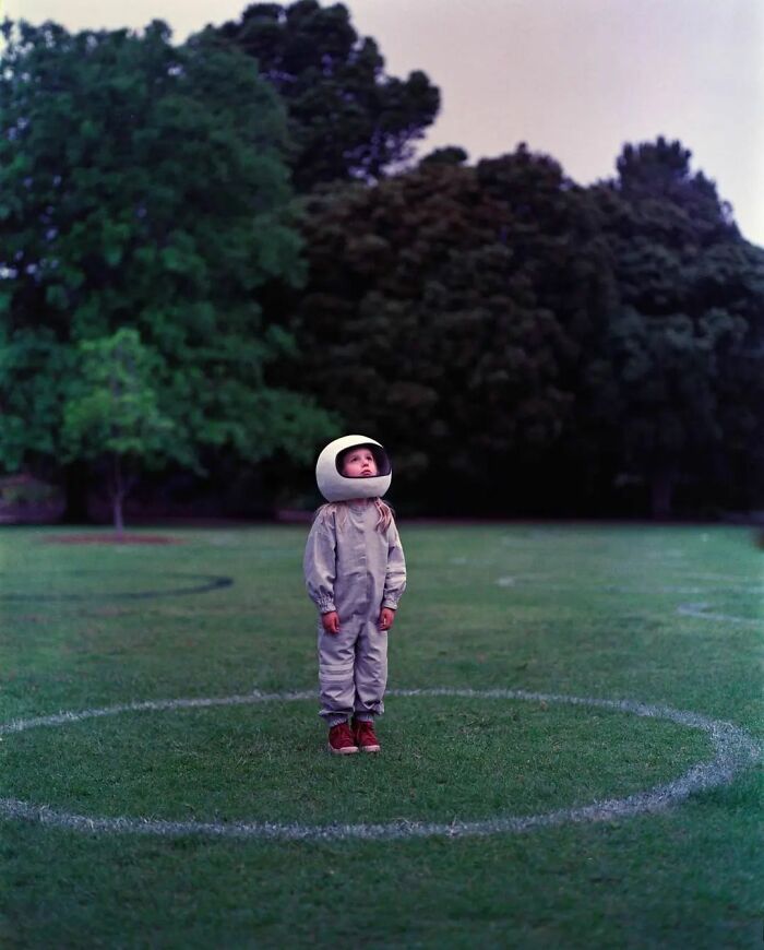 Child in an astronaut suit stands on grass, looking up, surrounded by circular marks—amusing photo shared on Instagram.