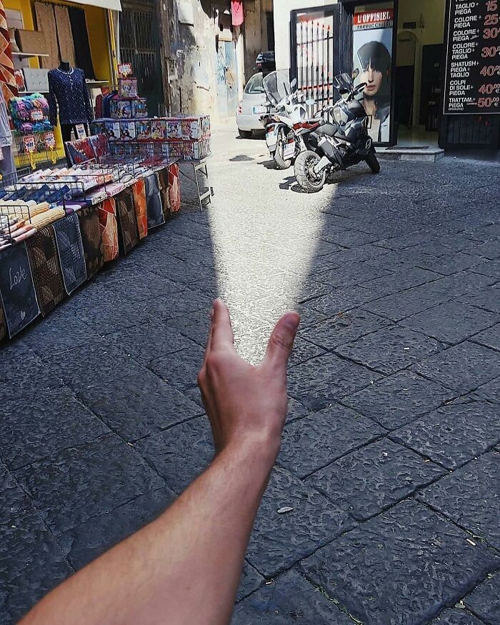 Hand reaching into a sunlit alley, creating an amusing illusion of controlling light in the street.