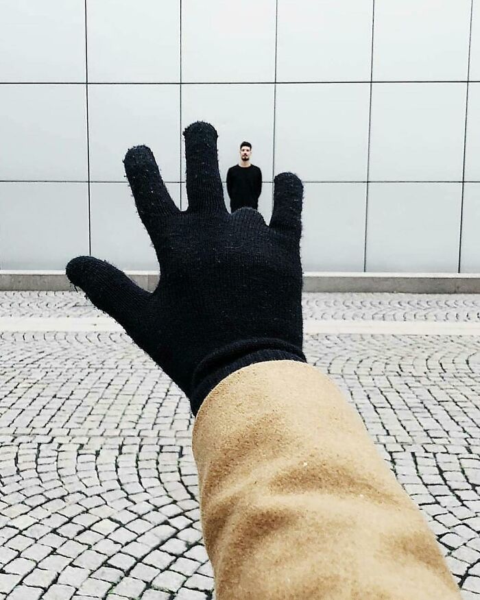 Gloved hand visually "holding" a distant person on cobblestone street, creating an amusing optical illusion.