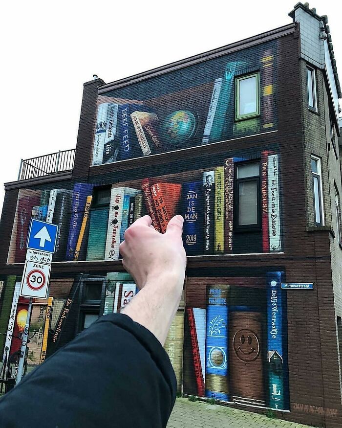 Street art mural of books on a building, person giving a thumbs-up; amusing photo from popular Instagram page.