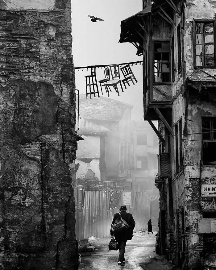 Man walking in a misty alley with hanging chairs overhead, in an amusing Instagram photo with over 85K followers.
