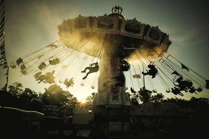 Amusing photo of a swinging carousel at sunset, with riders silhouetted against the sunlit sky.