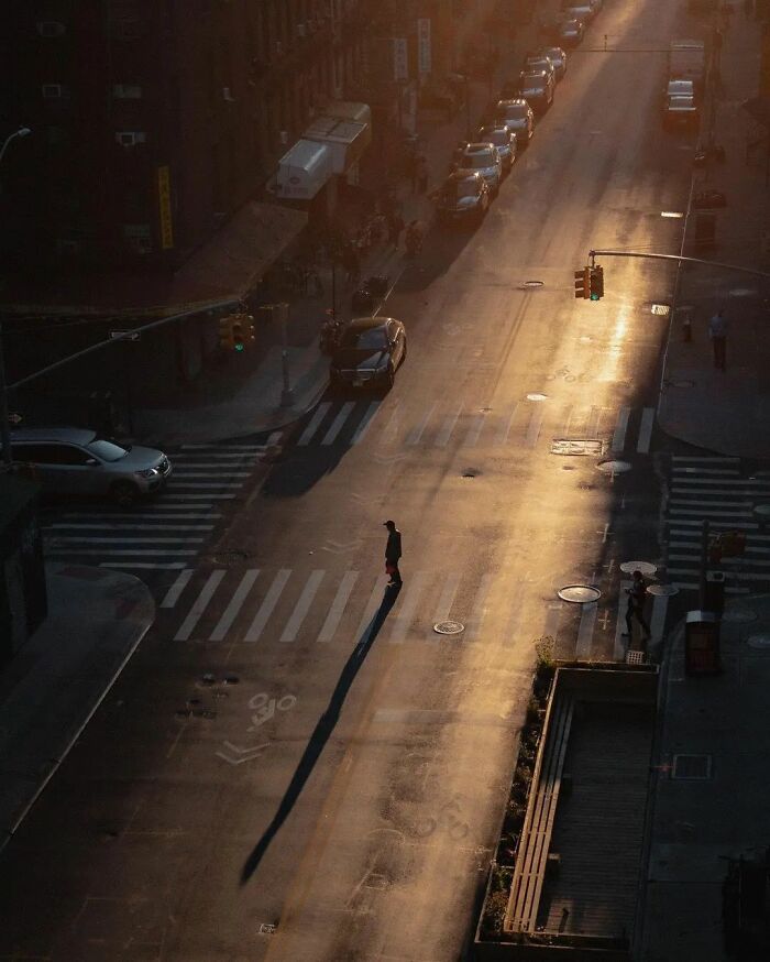 A person crossing an empty street at sunset, creating a long shadow, capturing an amusing urban moment.