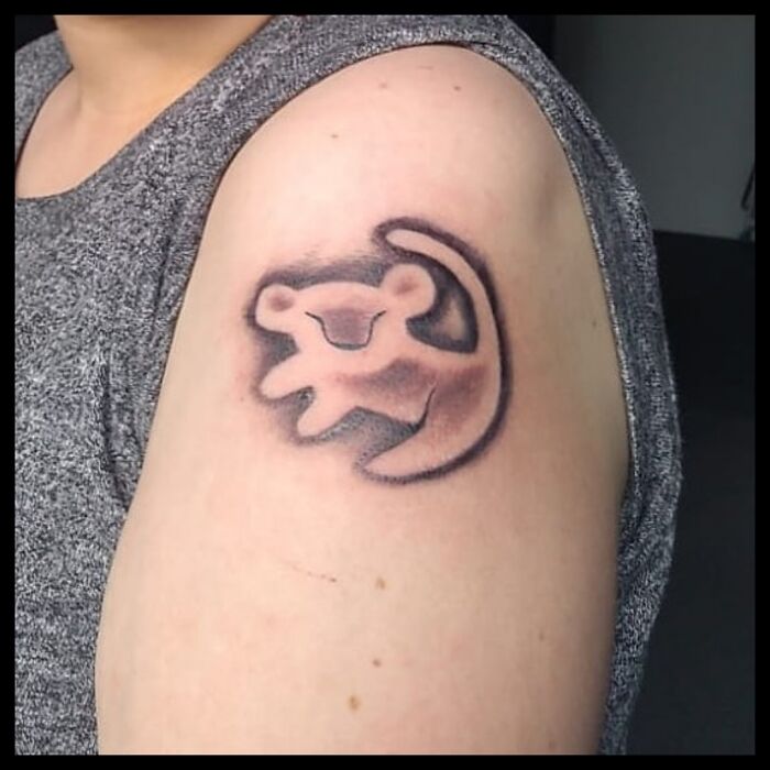 Tattoo of a stylized Simba design on a person's upper arm.