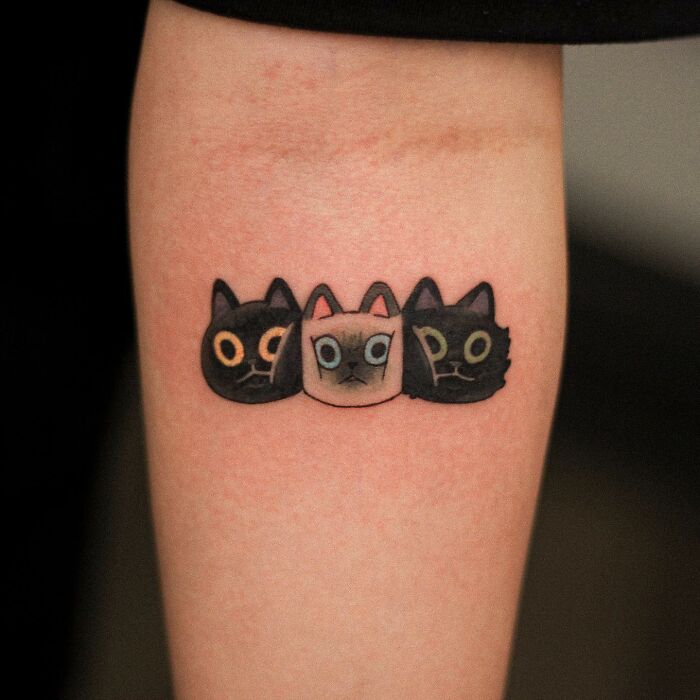 Adorable animal-themed tattoo of three cartoon cat faces on an arm.
