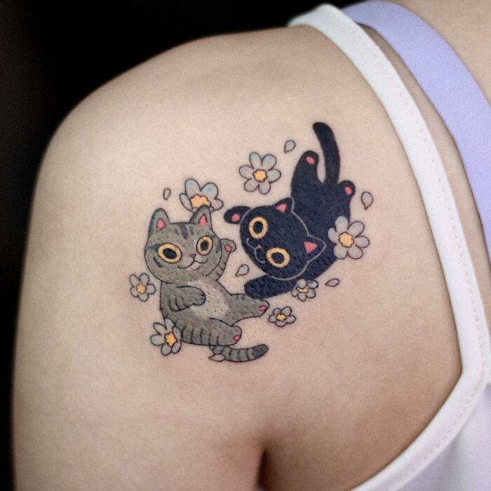 Adorable animal-themed tattoo of two playful cats surrounded by flowers on a person's shoulder.