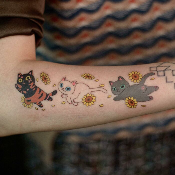 Adorable animal-themed tattoo featuring playful cats and flowers on an arm.