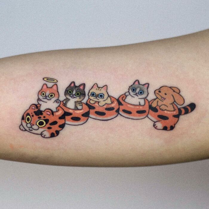 Adorable animal-themed tattoo featuring cute cats and a bunny in tiger-striped cups on an arm.