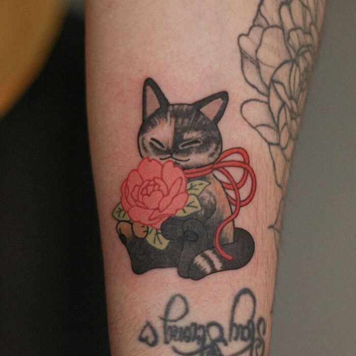 Adorable animal-themed tattoo of a cat with a flower and bow on a person's arm.