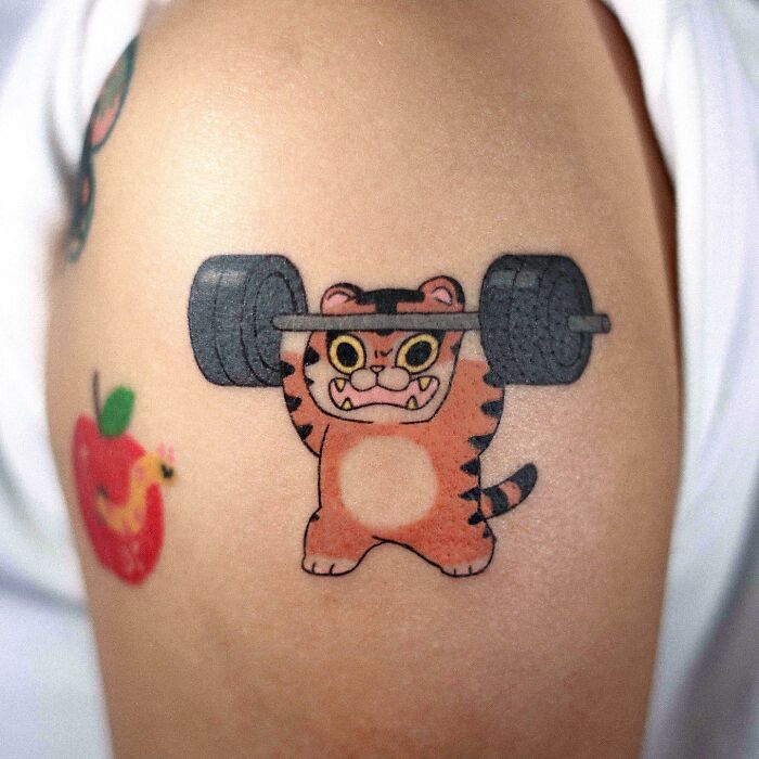 Tattoo of a cartoon tiger lifting weights on skin, showcasing adorable animal-themed art.