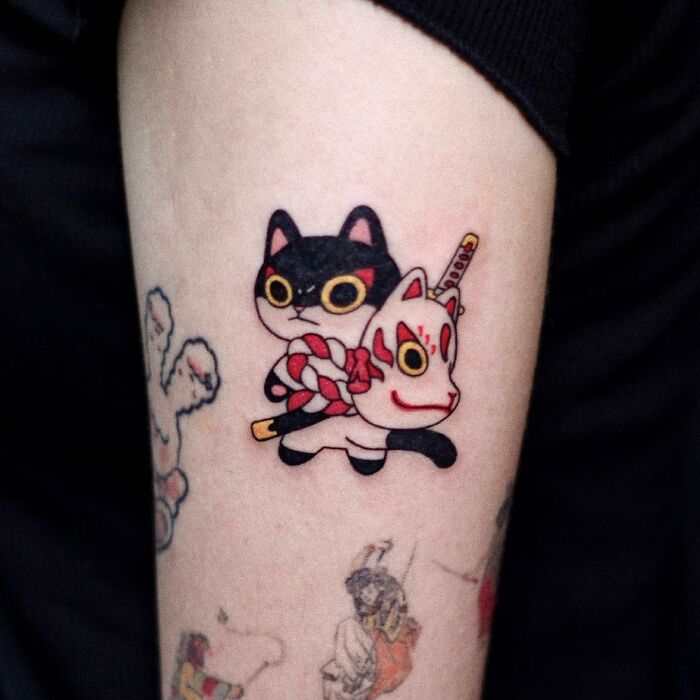 Adorable animal-themed tattoo of black cat in mask and red rope on arm.