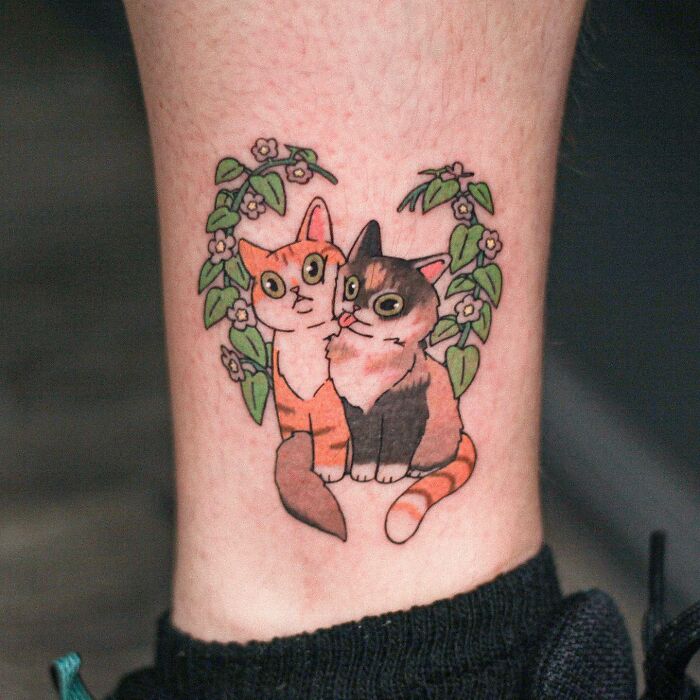 Adorable tattoo of two cats surrounded by floral vines, showcasing animal-themed design.