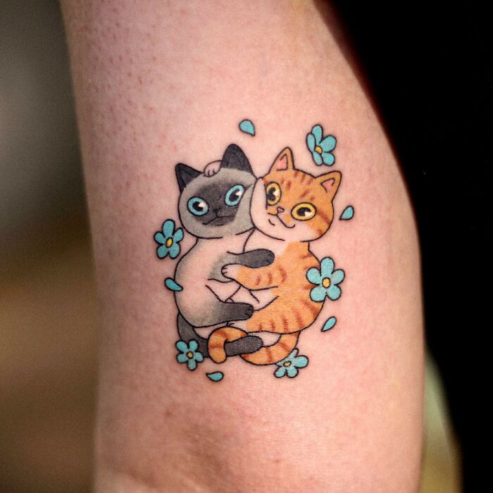 Adorable animal-themed tattoo featuring hugging cats surrounded by blue flowers.