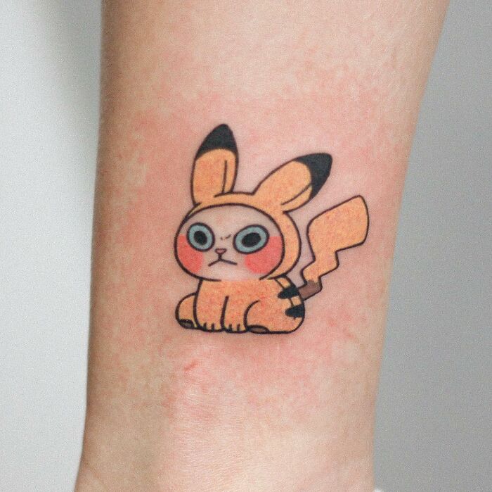 Adorable animal-themed tattoo of a cartoon-style creature with large eyes and a lightning tail.
