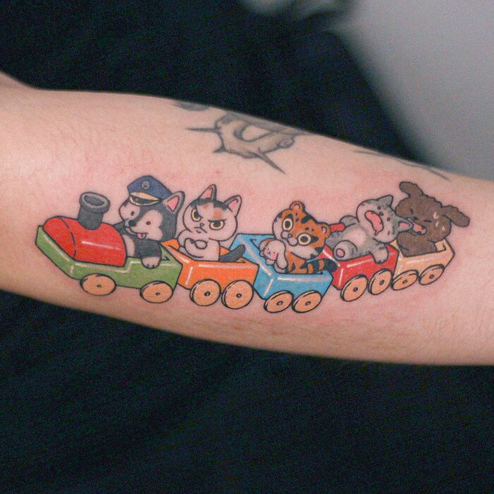 Adorable animal-themed tattoo of cats and dogs in a colorful train on a person's forearm.
