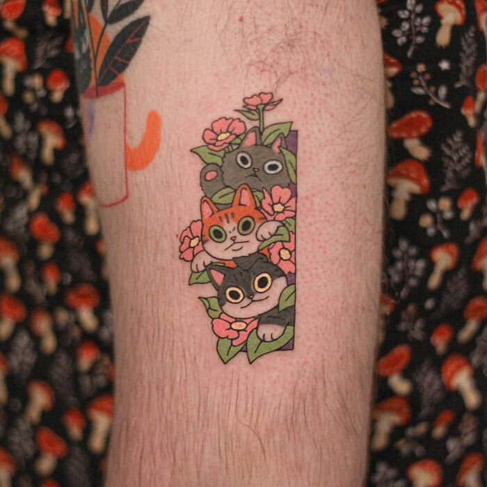 Adorable animal-themed tattoo of colorful cartoon cats with flowers on an arm.