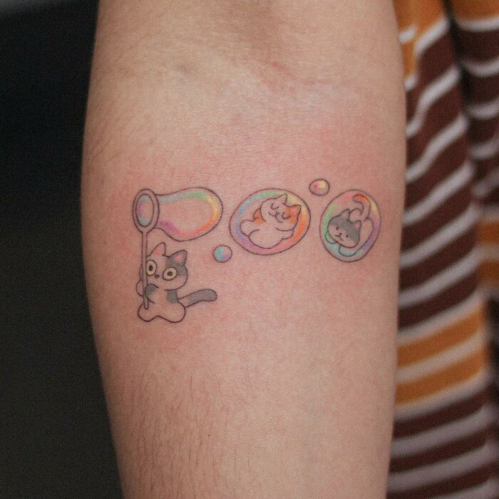 Adorable animal-themed tattoo featuring cartoon cats in colorful bubbles on an arm.