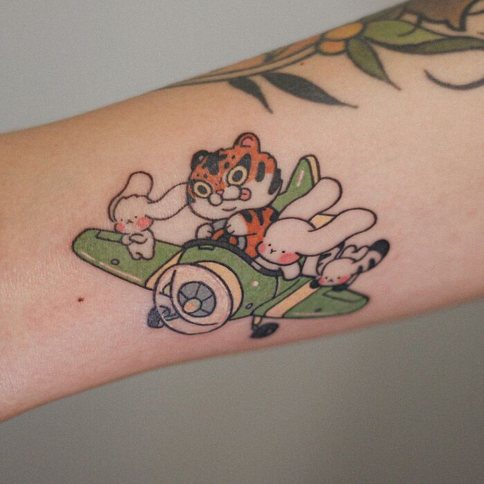 Adorable animal-themed tattoo featuring a cartoon tiger and rabbits in an airplane on an arm.