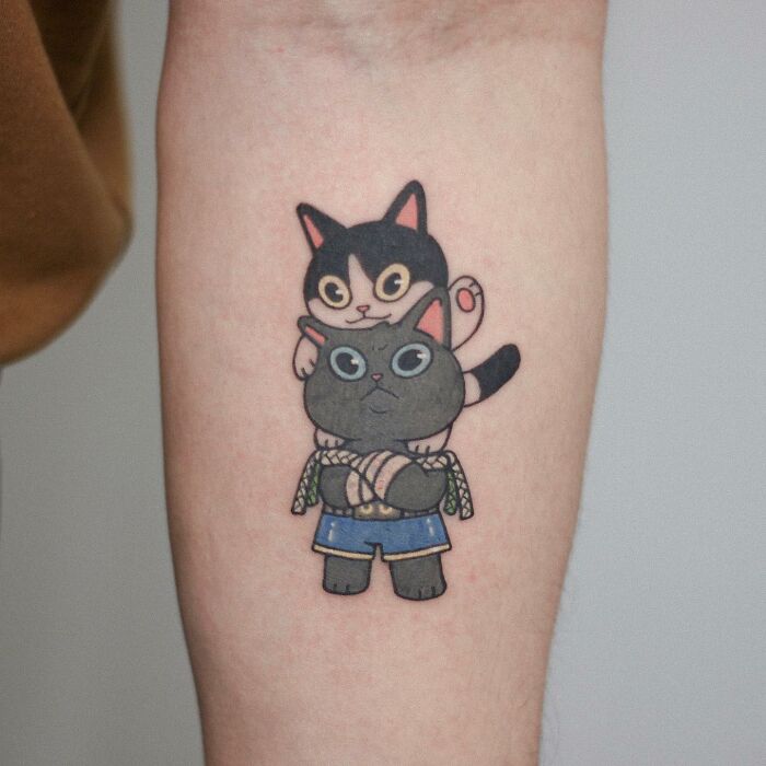 Tattoo of two cute cats stacked on an arm, showcasing adorable animal-themed design.