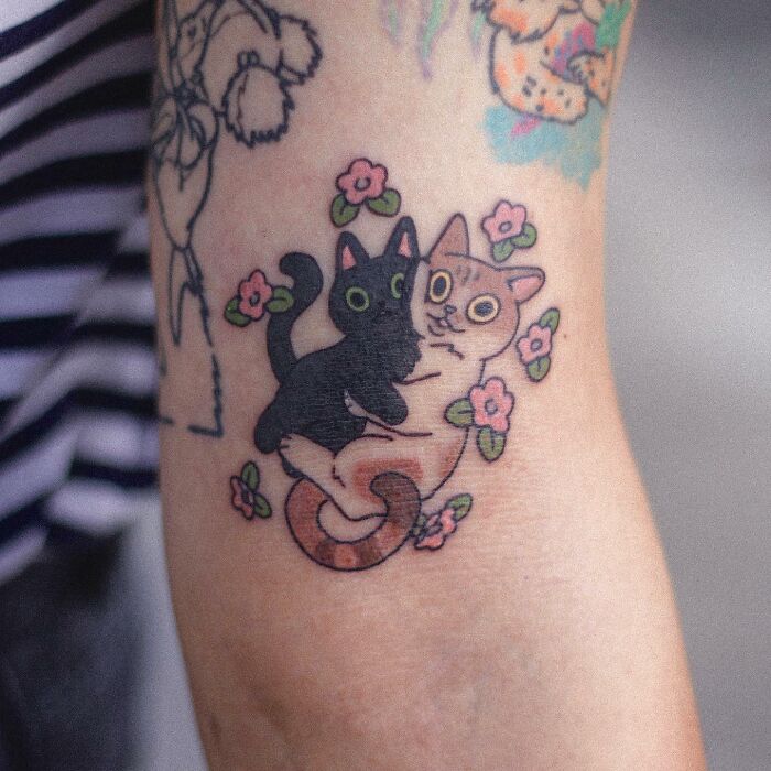 Adorable animal-themed tattoo of hugging cats surrounded by flowers.
