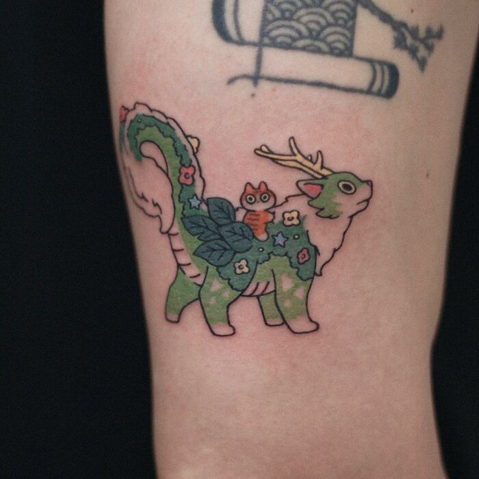Tattoo of a green animal with flowers and antlers on skin, showcasing an adorable animal-themed design.