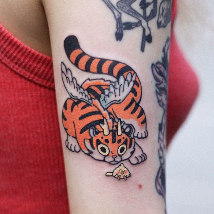 Tattoo of a whimsical orange tiger with wings, showcasing an adorable animal-themed design on an arm.