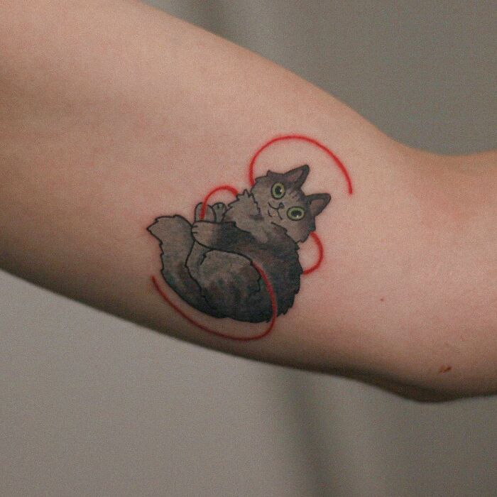 Adorable cat-themed tattoo on arm with red string design.
