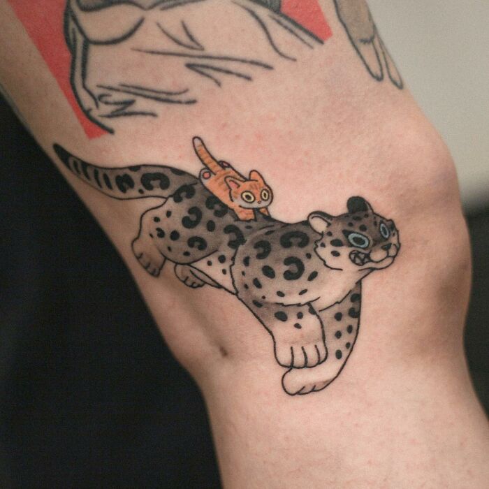 Adorable animal-themed tattoo of a cartoon snow leopard with a small orange cat on its back.