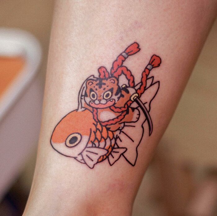 Adorable animal-themed tattoo featuring a cartoon tiger riding a goldfish.