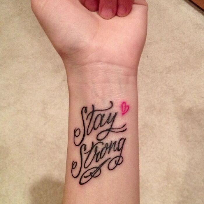 Wrist tattoo with "Stay Strong" and a pink heart, showcasing a meaningful statement.