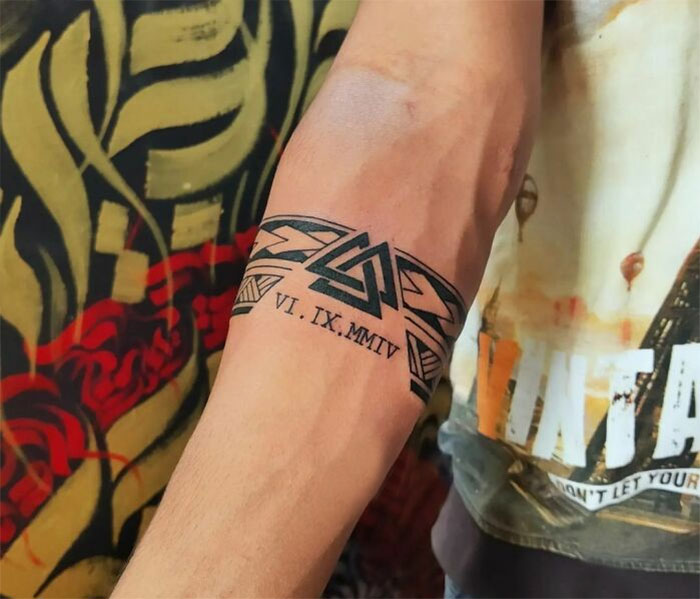 Geometric armband tattoo design with Roman numerals on a man's arm, close-up view.