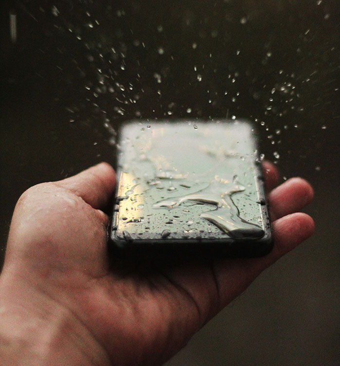 Man holding a phone and there are splash of water on it