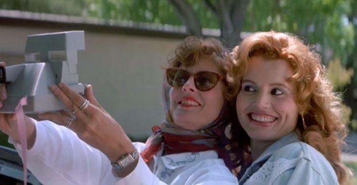 Two women smiling while taking a selfie, representing iconic best friend duos in a joyful moment outdoors.