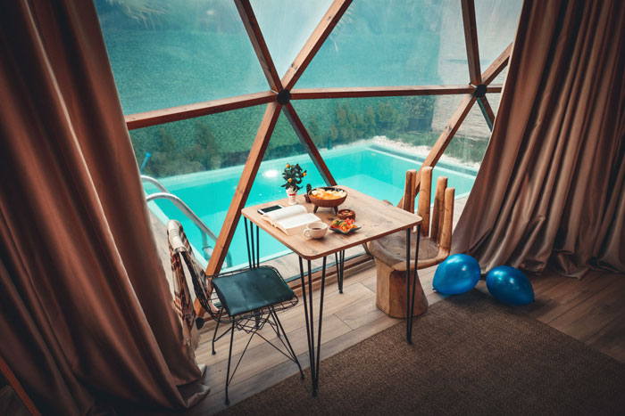 Cozy room decor with a wooden table and chair by a pool, featuring elegant curtains and geometric window design.