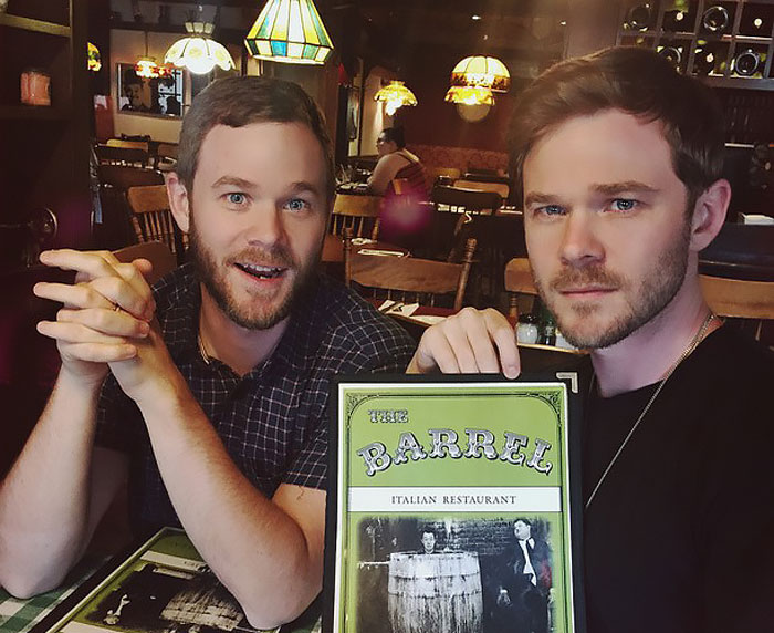 Two celebrity twins sitting in a restaurant, one holding a menu, showcasing the appeal of celebrity twins pairs.