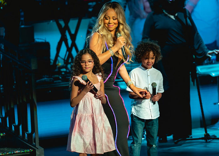 Female celebrity singer performing on stage with her young twin children holding microphones during a live concert.