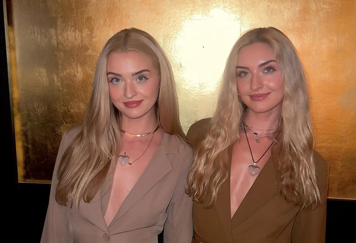 Two celebrity twins with long blonde hair wearing brown blazers, posing against a gold background for celebrity twins.