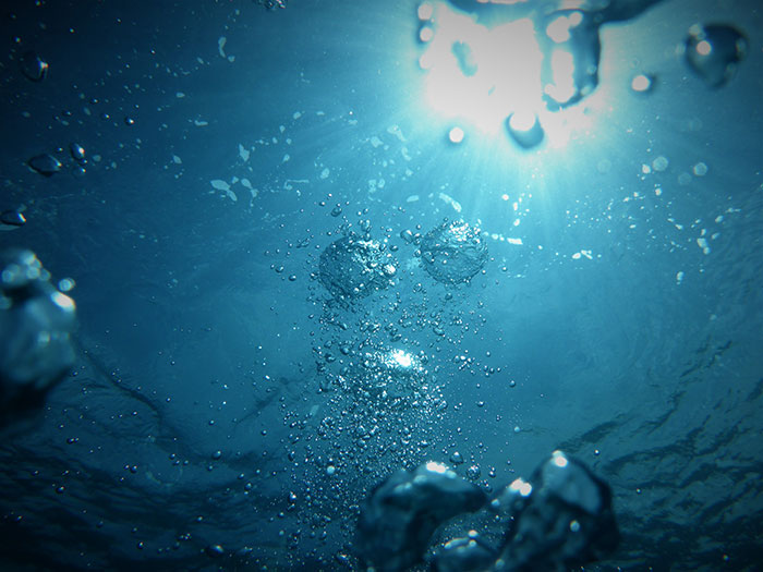Underwater view of water and bubbles demonstrating physics concepts related to fluid dynamics and gas behavior in liquids.