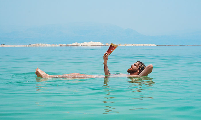 Person lying in the Dead Sea, floating effortlessly while reading, showcasing physics principles in natural water buoyancy.