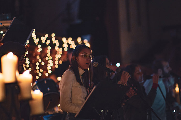 Woman singing on stage, exploring fun hobbies, surrounded by candlelight and festive decorations.
