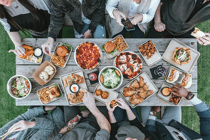 Group enjoying fun hobbies, sharing diverse food at a table outdoors.