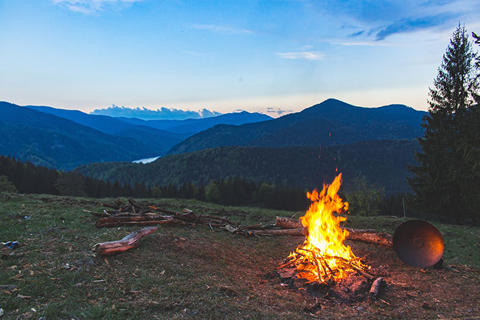 Bonfire on a green grass field with mountains in the background, perfect for trying out fun hobbies outdoors.