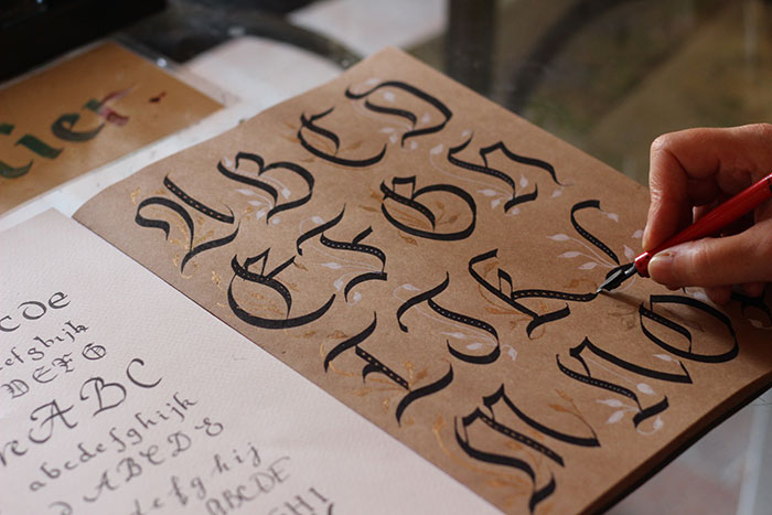 Handwriting hobby: person's hand practicing calligraphy with a red pen on a brown paper.