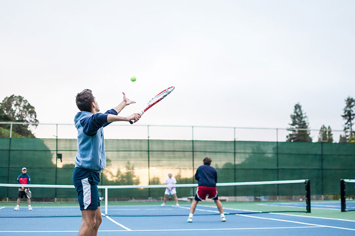 People enjoying one of many fun hobbies, playing tennis on a blue court under a cloudy sky.