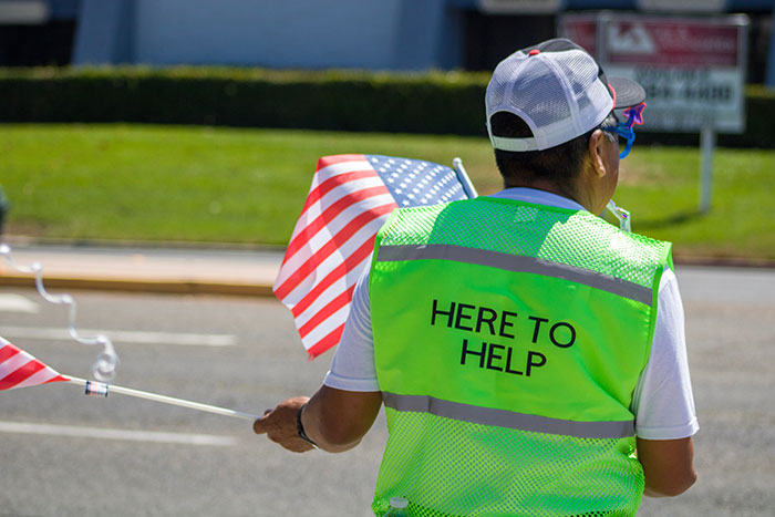 Man in green waistcoat with American flag, assisting in street.