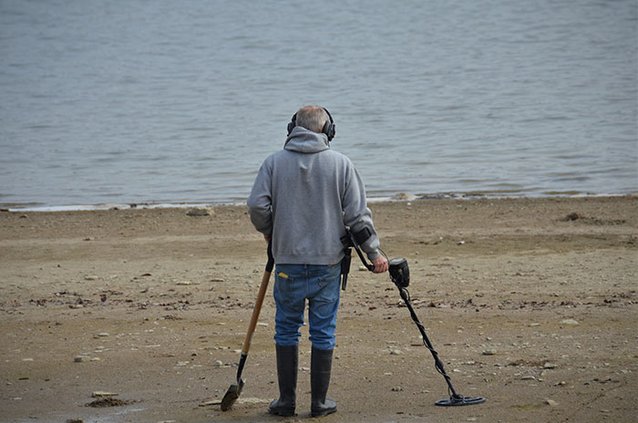 Man using metal detector on the beach, exploring fun hobbies near the sea.