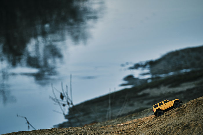 Yellow toy truck on sandy slope by a lake, highlighting fun hobbies in outdoor settings.